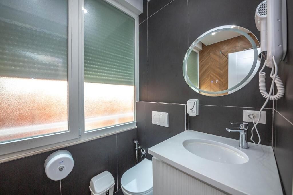 A modern bathroom with a large window, a round mirror, a hairdryer, and a toilet.