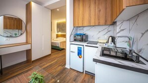 Eine kompakte Küche mit Mikrowelle, Spüle und kleinem Kühlschrank. Oberhalb der Spüle befindet sich ein Holzschrank und an der Wand ein Spiegel.