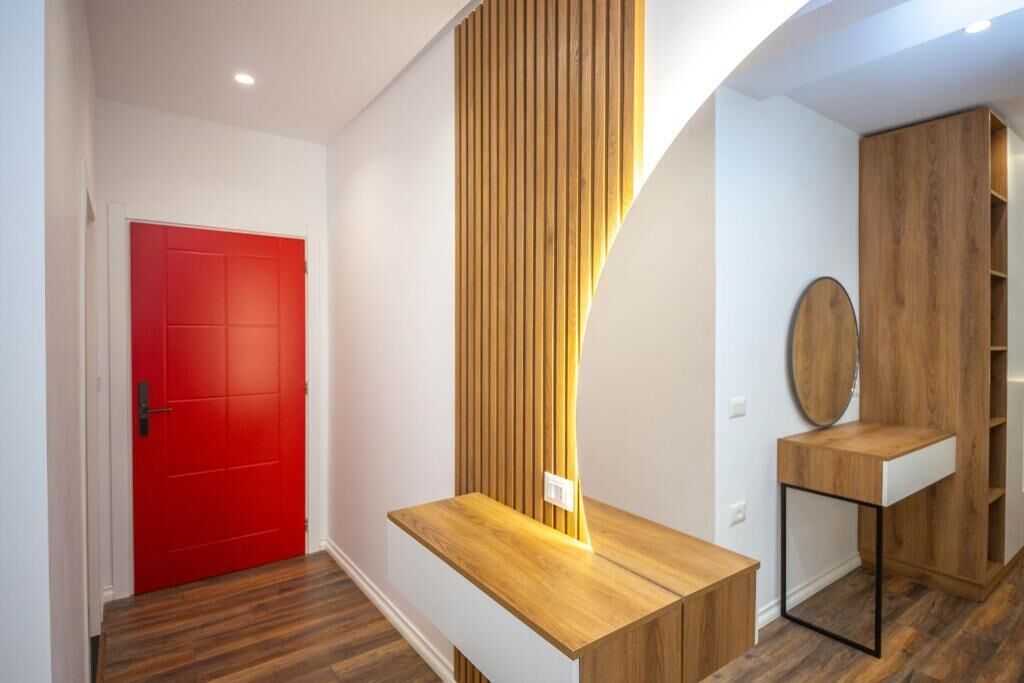 Un pasillo moderno con una puerta roja, paneles de madera y una pequeña mesa de madera con un espejo.
