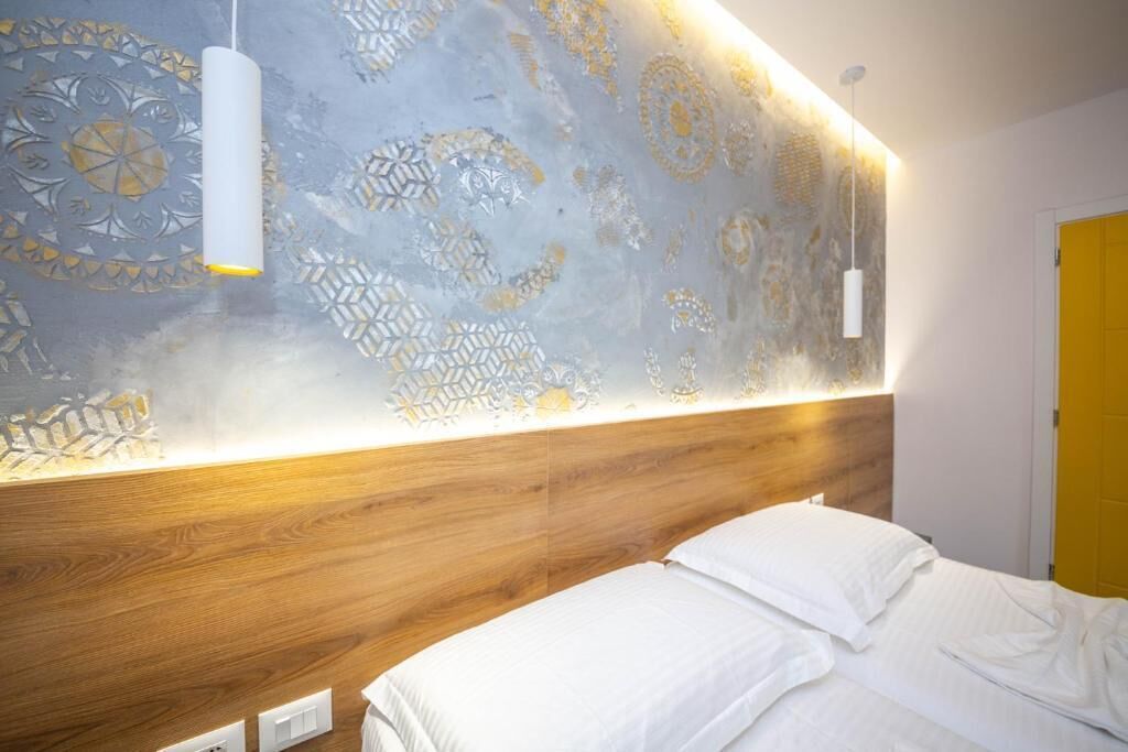 Una camera d'albergo moderna con testiera in legno, parete decorata e letto con lenzuola bianche.