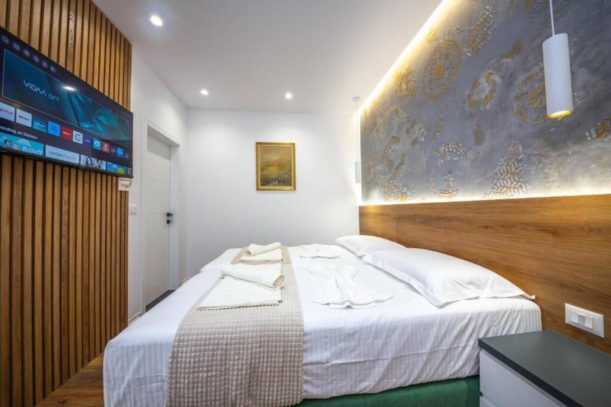 Une chambre d’hôtel avec une tête de lit en bois, un téléviseur à écran plat fixé au mur, un tableau au-dessus du lit et une table de chevet avec une lampe.