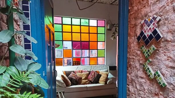 A cozy room with a colorful stained glass window, a cushioned bench, and a textured wall.