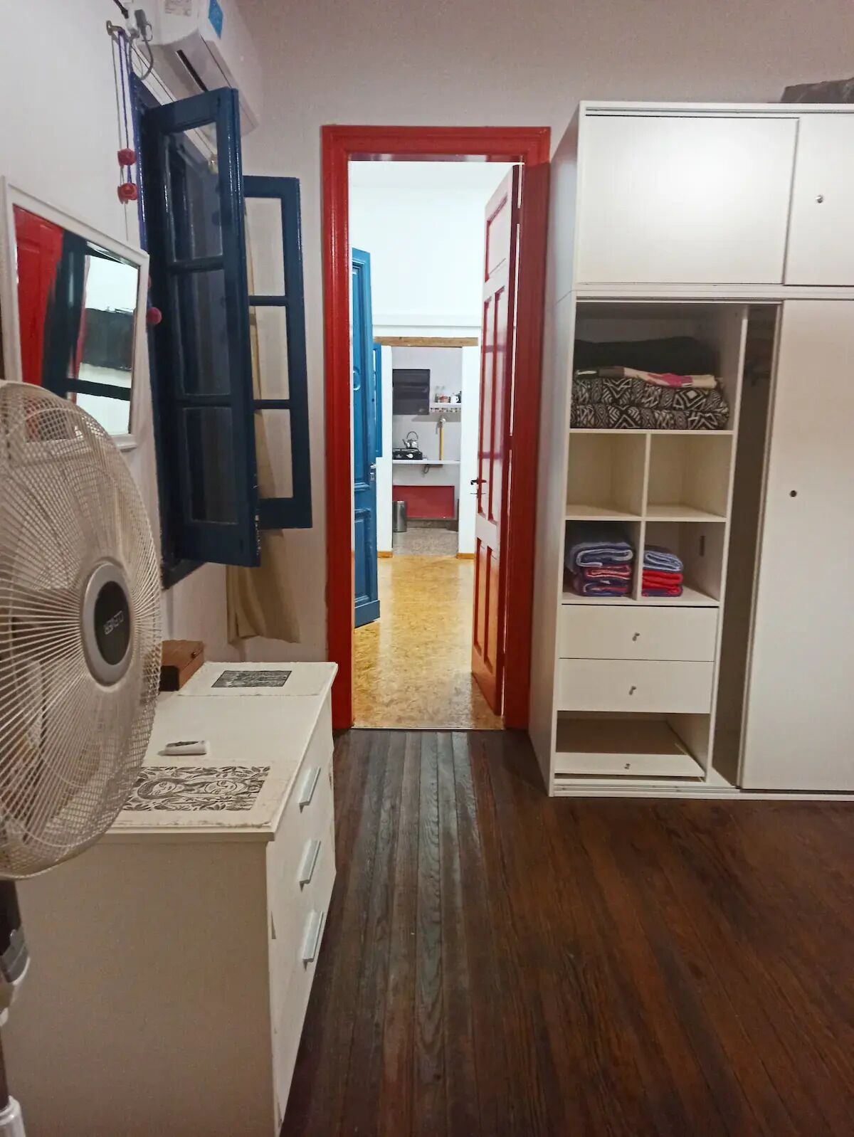 A narrow hallway with a fan, a wardrobe, and a kitchen area visible through an open door.