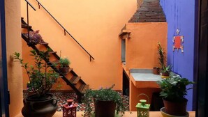 A narrow alleyway with a staircase leading up, potted plants, and a window with a view of the interior.