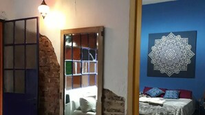 A room with a brick wall, a mirror, a blue wall with a mandala artwork, and a bed with pillows.