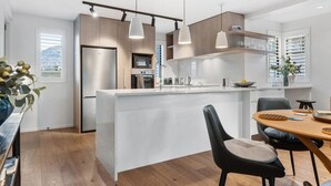 A modern kitchen with a central island, pendant lighting, and built-in appliances. - Wanaka Station Apartment (Wānaka)
