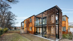 A modern two-story house with a wooden exterior, large windows, and a balcony. - Wanaka Station Apartment (Wānaka)