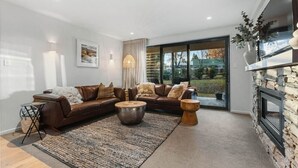 A modern living room with a brown leather sofa, a round coffee table, and a stone fireplace. - Wanaka Station Apartment (Wānaka)