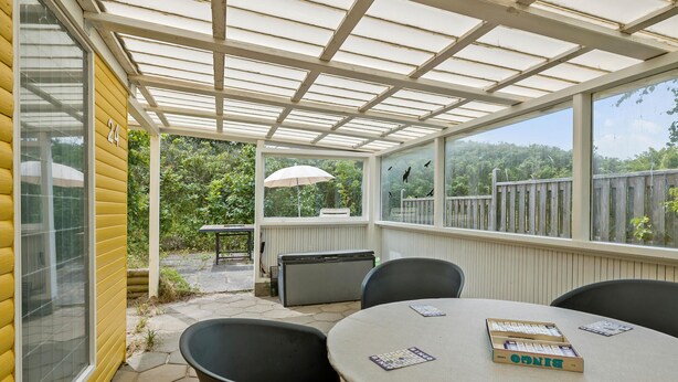 Eine überdachte Terrasse mit Tisch und Stühlen, ein Fenster mit Blick auf Bäume und die Zahl 24 an der Wand.