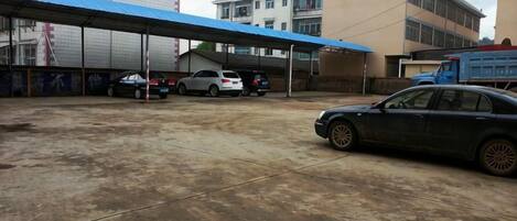 A parking area with cars, a covered structure, and buildings in the background.