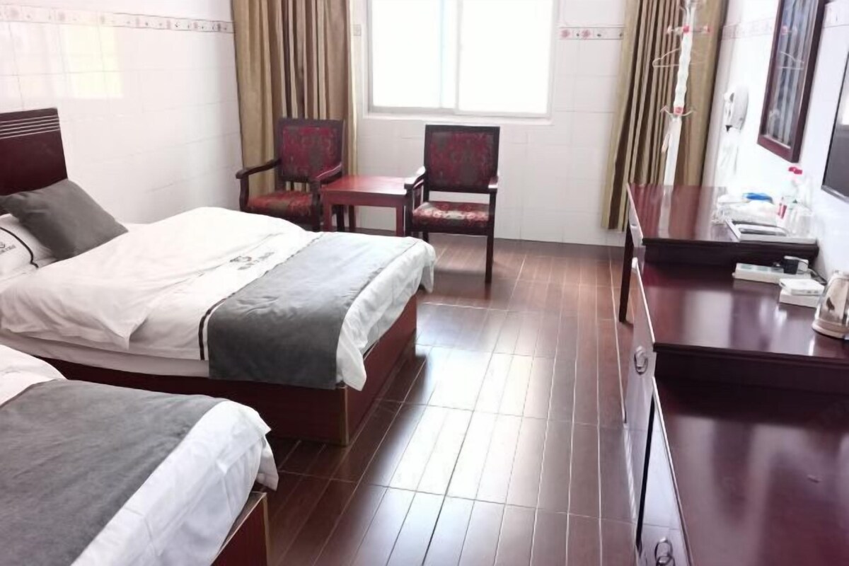 Quarto de hotel com duas camas, uma escrivaninha, uma cadeira e uma televisão.