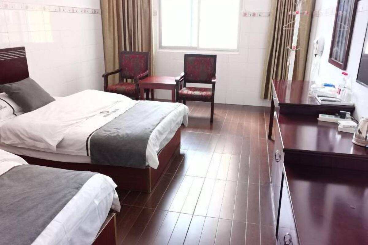 Ein Hotelzimmer mit zwei Betten, einem Schreibtisch, einem Sessel, einem Fernseher und einem Fenster mit Vorhängen.