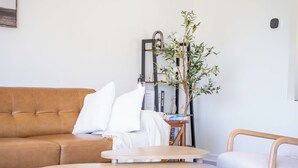 A living room with a brown leather sofa, a white armchair, a small round wooden table, and a bookshelf with books and a potted plant. - Spacious 5B2B home 5 min to airport with AC, Game Room, Sleeps 16 (SeaTac)