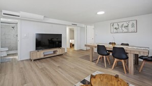 A modern living room with a TV, dining table, and chairs. - Spacious 5B2B home 5 min to airport with AC, Game Room, Sleeps 16 (SeaTac)