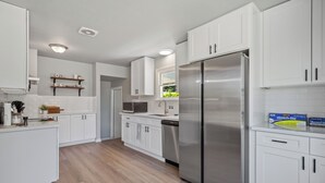 A modern kitchen with white cabinets, a stainless steel refrigerator, and wooden flooring. - Spacious 5B2B home 5 min to airport with AC, Game Room, Sleeps 16 (SeaTac)