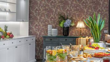 A well-lit room with a dining table set for a buffet, a decorative hanging light fixture, and a floral wallpaper pattern.