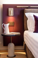 Camera d'albergo moderna con un letto, un comodino con un boccale bianco, un libro e un interruttore della luce a parete.