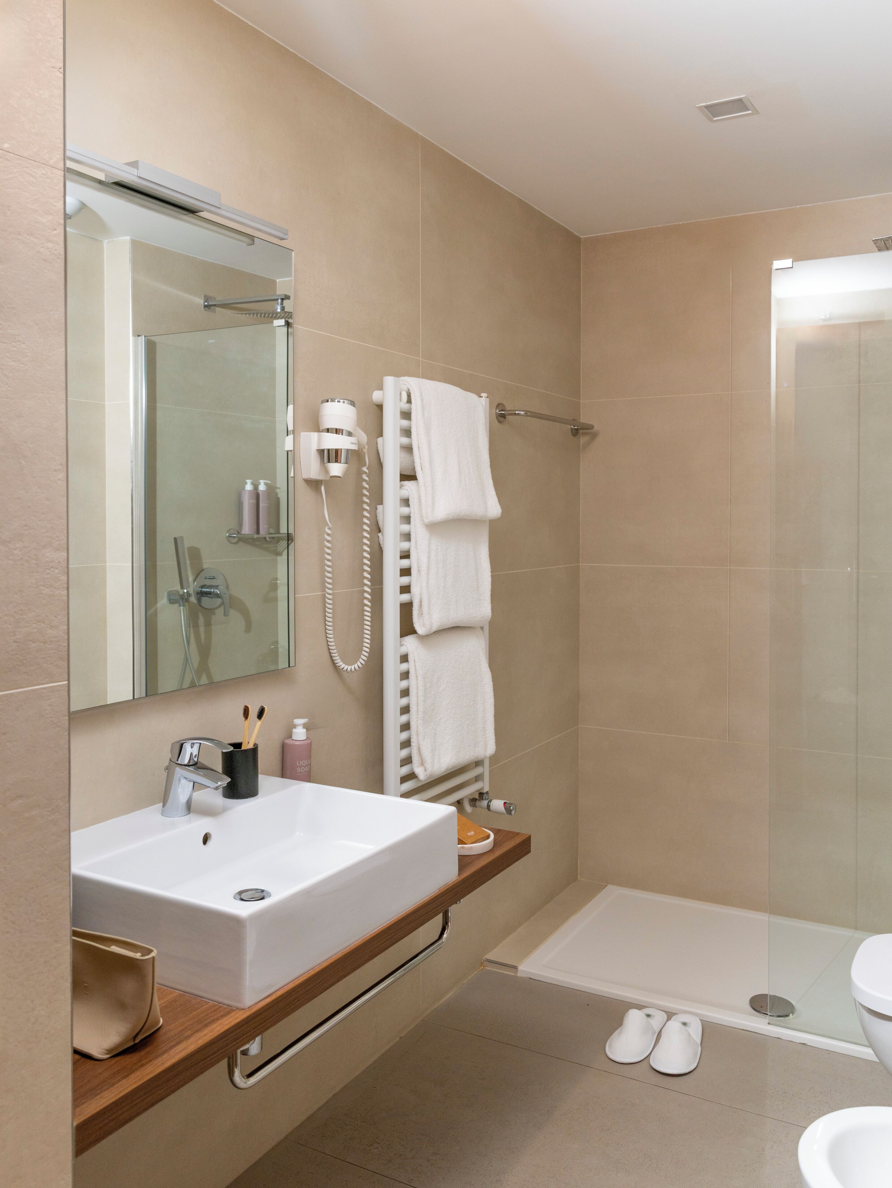 A modern bathroom with a large mirror, a white sink, a glass shower enclosure, and a toilet.
