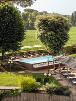 A swimming pool with lounge chairs and umbrellas, surrounded by a grassy area and trees.