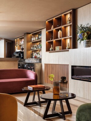 A modern living area with a sofa, a round table with a drink, and a bar area with shelves of bottles. - Adoro Hotel  (Rome)