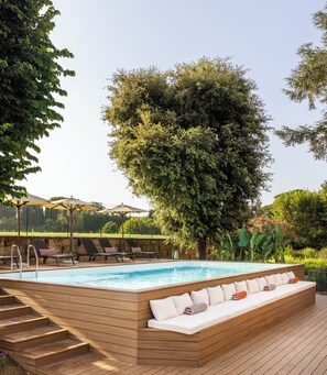 Une piscine dotée d’une terrasse en bois et d’un espace détente, entourée d’arbres et de verdure.