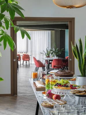 Un bufé de desayuno con diversos alimentos y vista al comedor, con sillas rojas y una mesa.