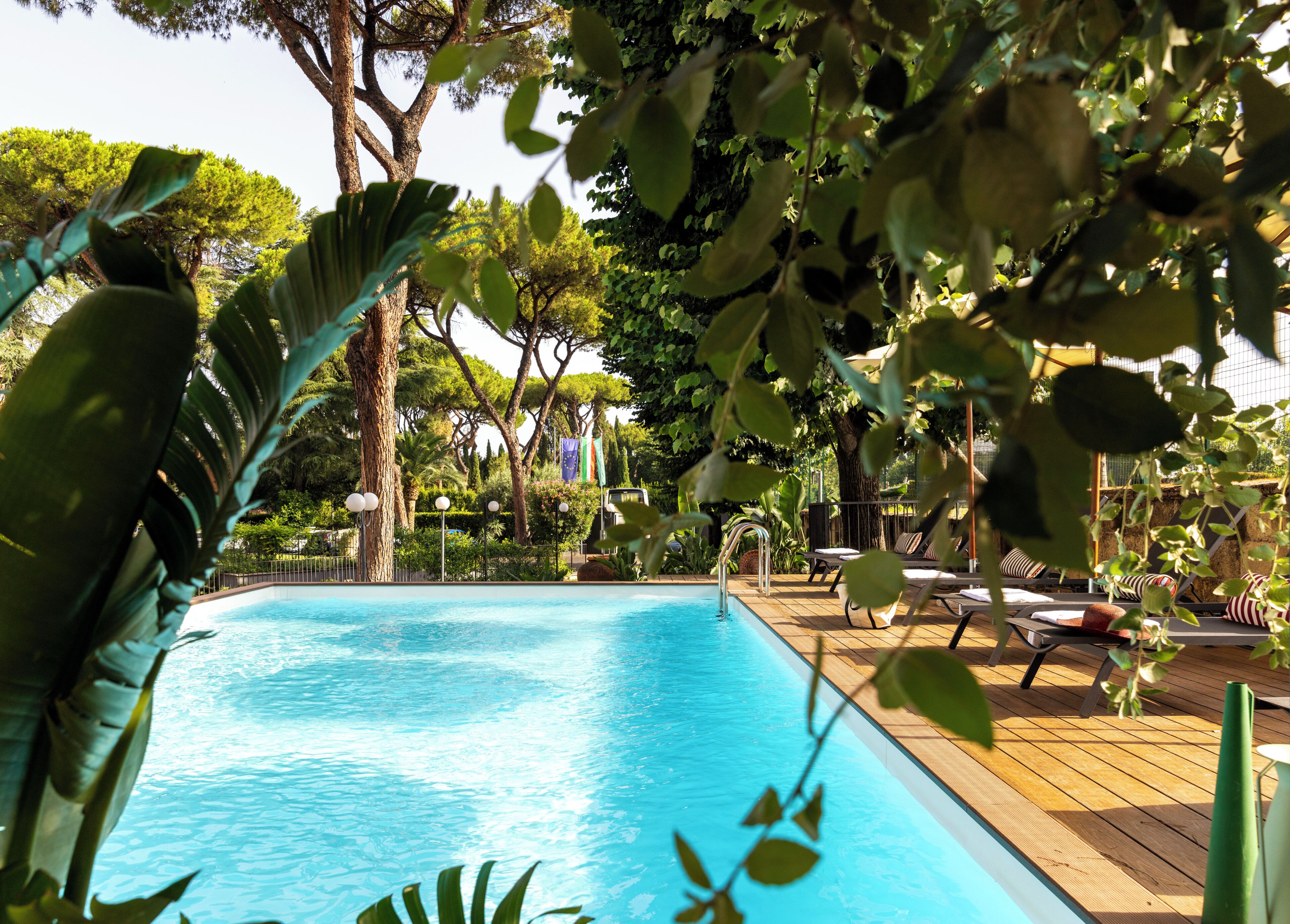 A swimming pool with lounge chairs and umbrellas, surrounded by trees and greenery.
