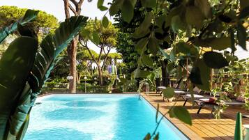 A swimming pool with lounge chairs and umbrellas, surrounded by trees and greenery.