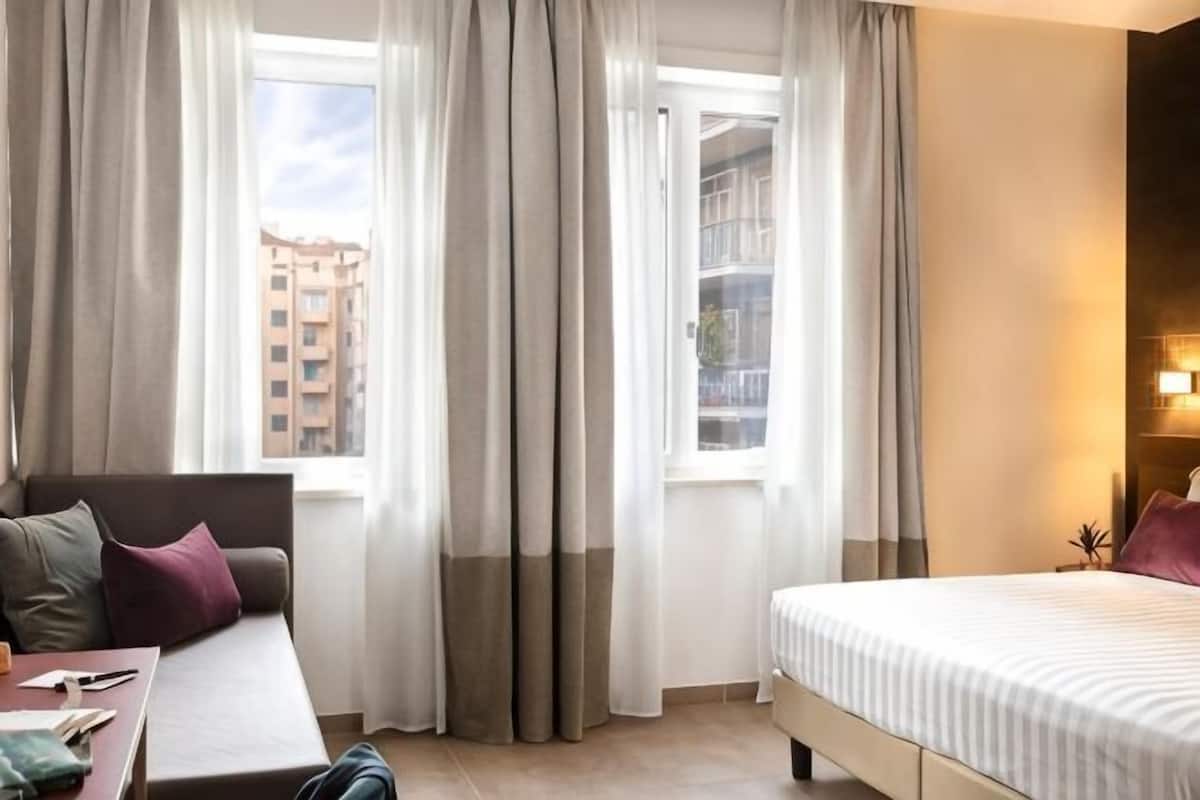 A hotel room with a bed, a sofa, a table, and curtains.
