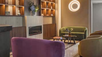 Een moderne woonkamer met een open haard, een groene bank, een paars voetenbankje en een houten boekenkast.