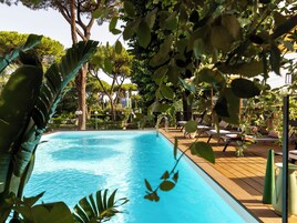 Una piscina con lettini e ombrelloni, circondata da alberi e piante.