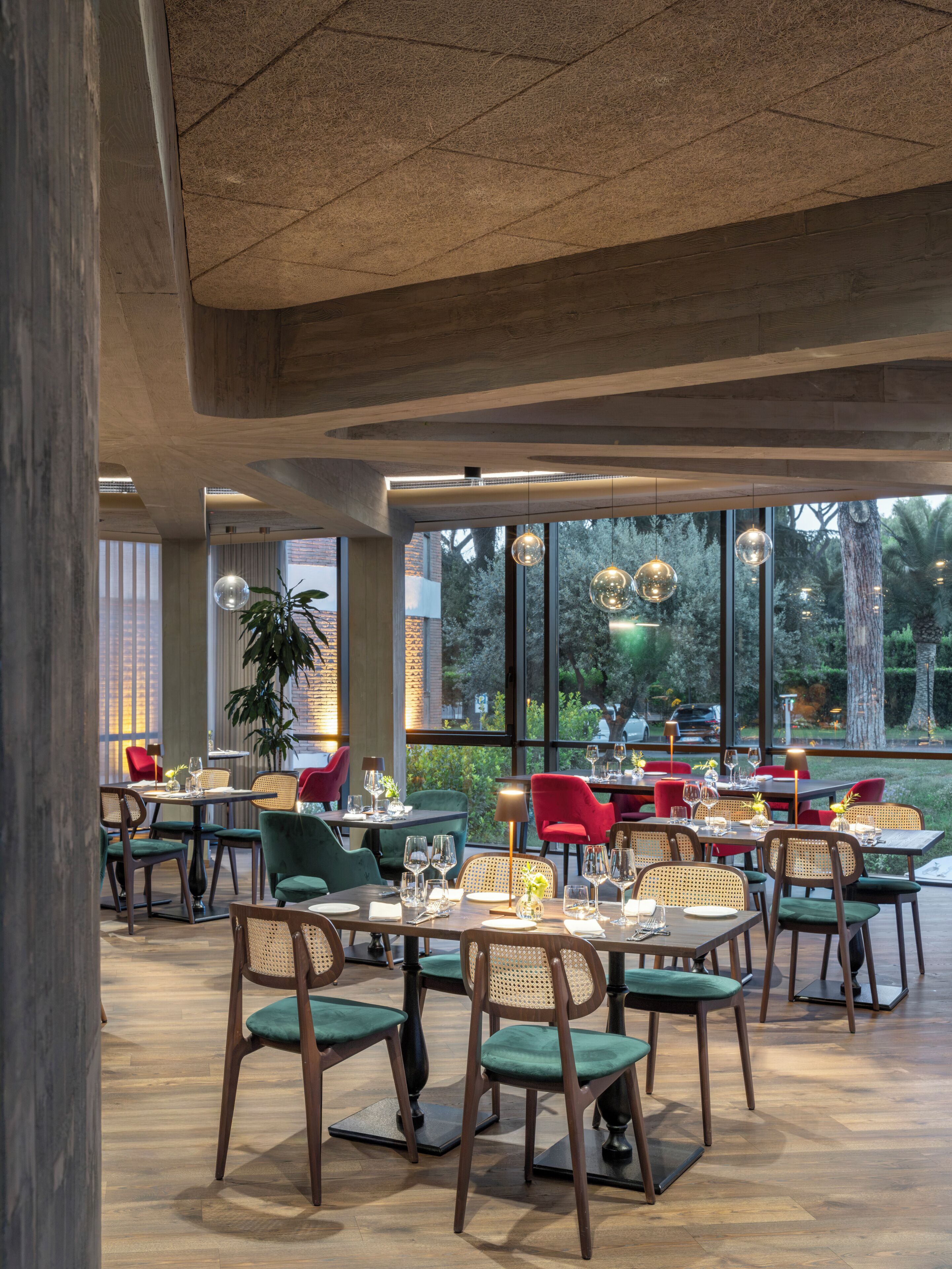 Een restaurant met een modern interieur, met houten tafels en stoelen, grote ramen en hangende, bolvormige lampen.