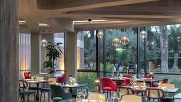 A restaurant with a modern interior, featuring wooden tables and chairs, large windows, and hanging spherical light fixtures.