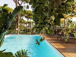 Una piscina con un pontile in legno, circondata da rigogliosa vegetazione e alberi.