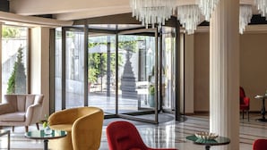 A spacious lobby with modern furniture, a large glass door leading outside, and a decorative chandelier. - Adoro Hotel  (Rome)