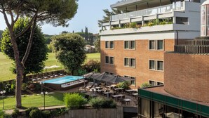 A rooftop pool area with outdoor seating and a view of a building with multiple windows. - Adoro Hotel  (Rome)