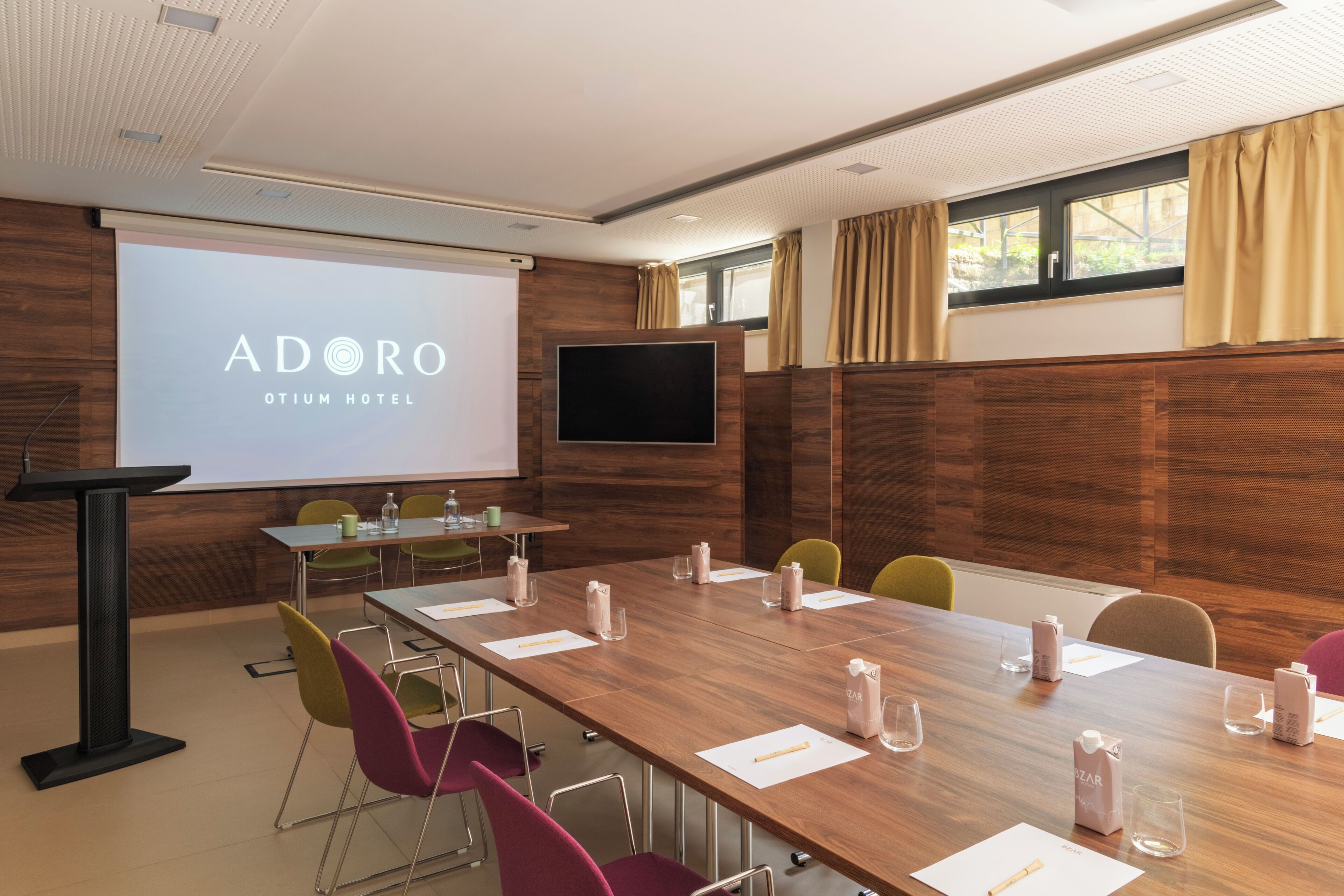 A conference room with a wooden table, chairs, a projector screen, and a television.