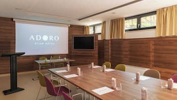 A conference room with a wooden table, chairs, a projector screen, and a television.