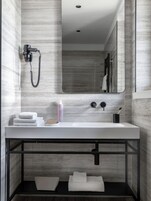 Un bagno moderno con un lavandino bianco, un soffione doccia a mano, un porta asciugamani e uno specchio.