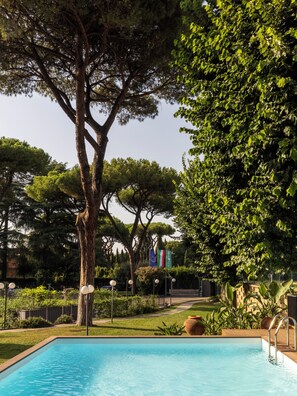 Une piscine entourée d’une végétation luxuriante et d’arbres, sous un ciel dégagé.