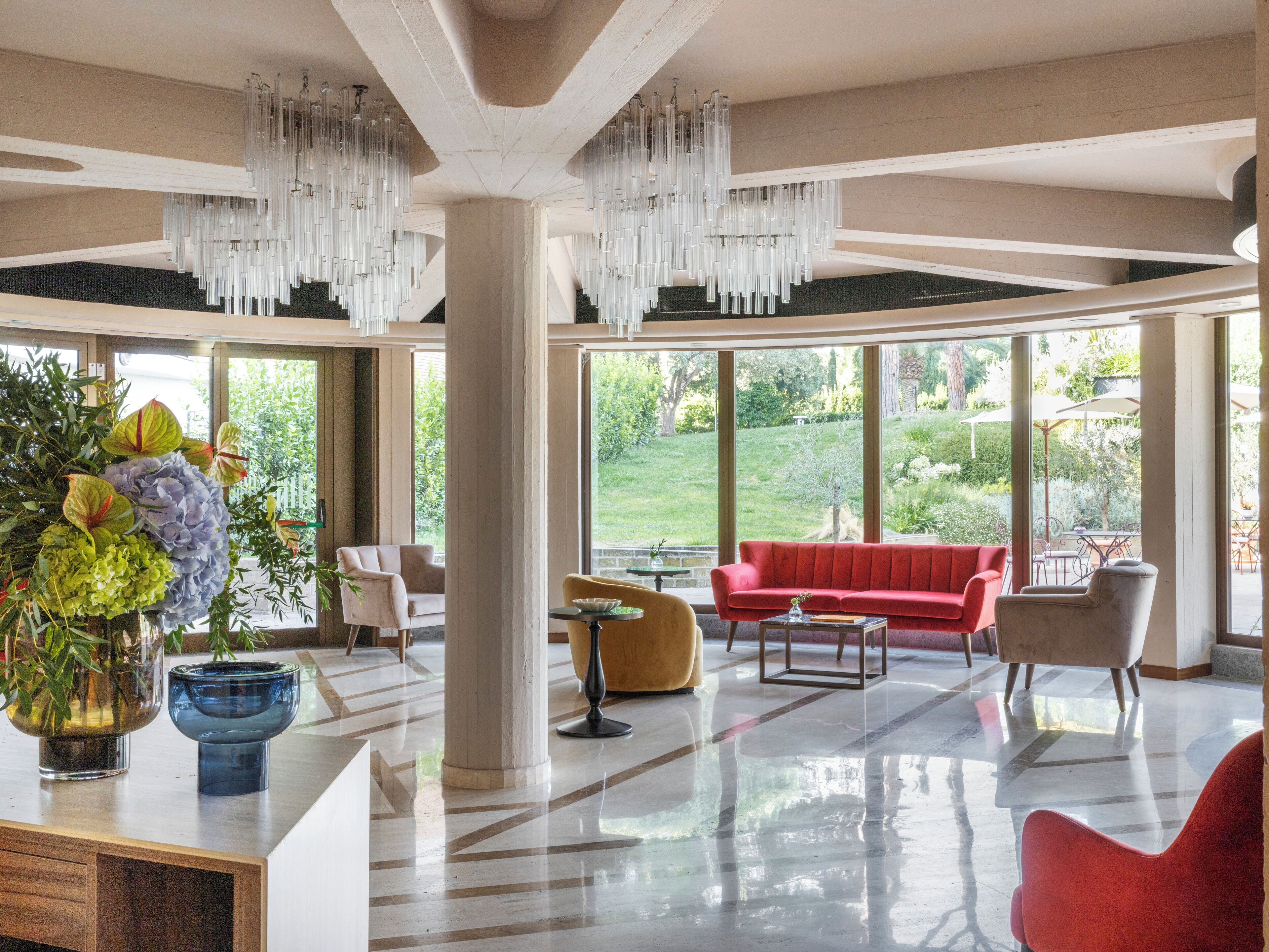 Una habitación amplia con un sofá rojo, una silla amarilla y un ventanal con vistas a un jardín.