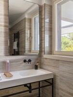 A bathroom with a white sink, a mirror, and a window.