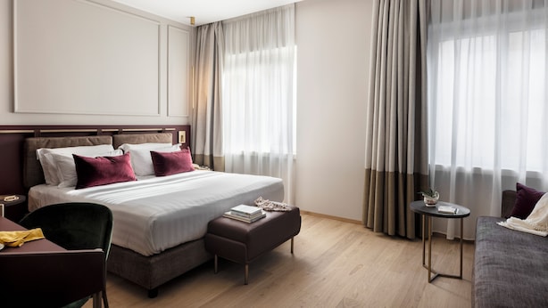 A modern hotel room with a large bed, a small table, a sofa, and a chair.