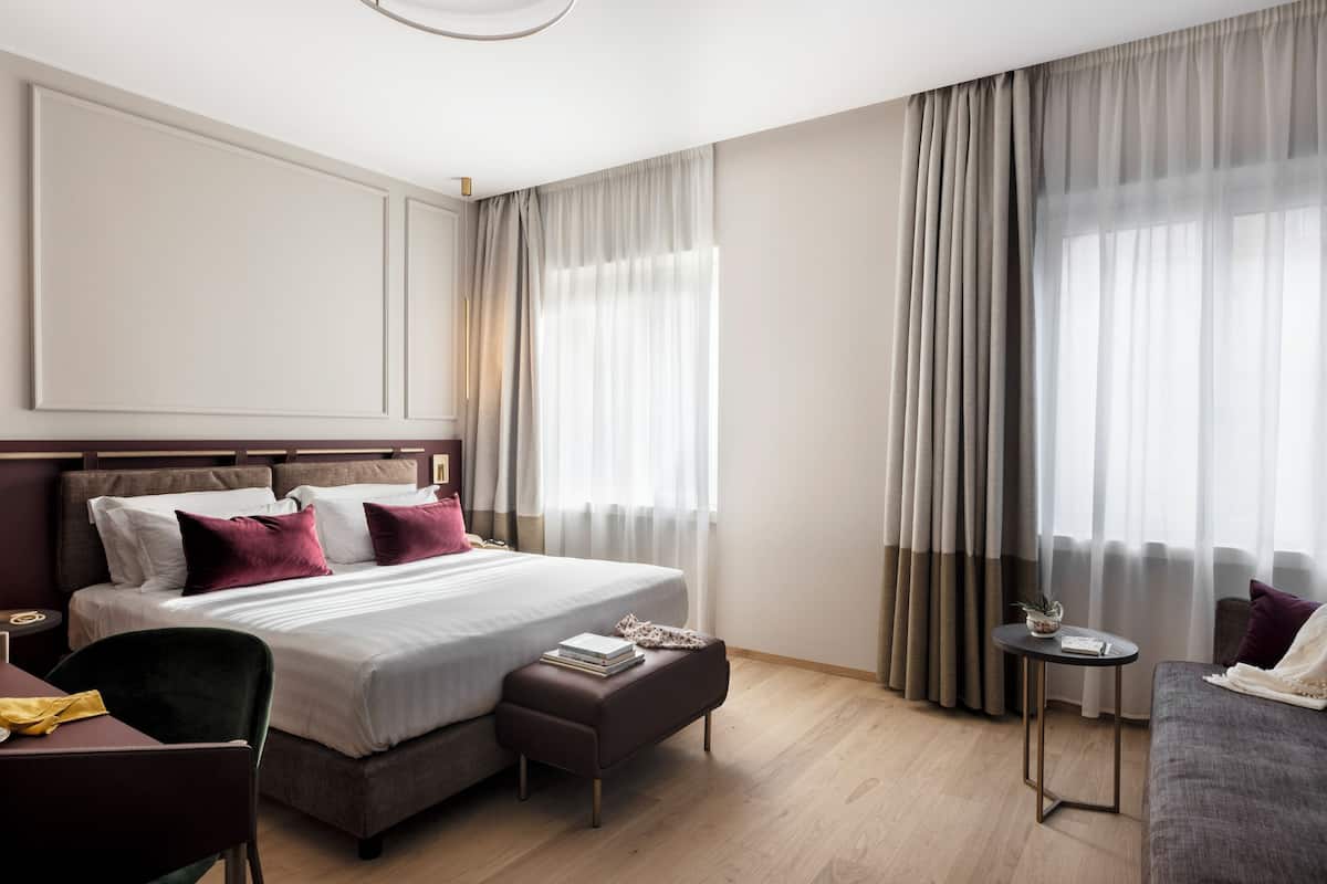 A modern hotel room with a large bed, a small table, a sofa, and a chair.