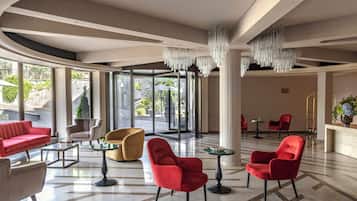 Un vestíbulo amplio con diseño moderno, que cuenta con un sofá rojo, un sillón amarillo y sillas rojas, con un gran ventanal que da al exterior.