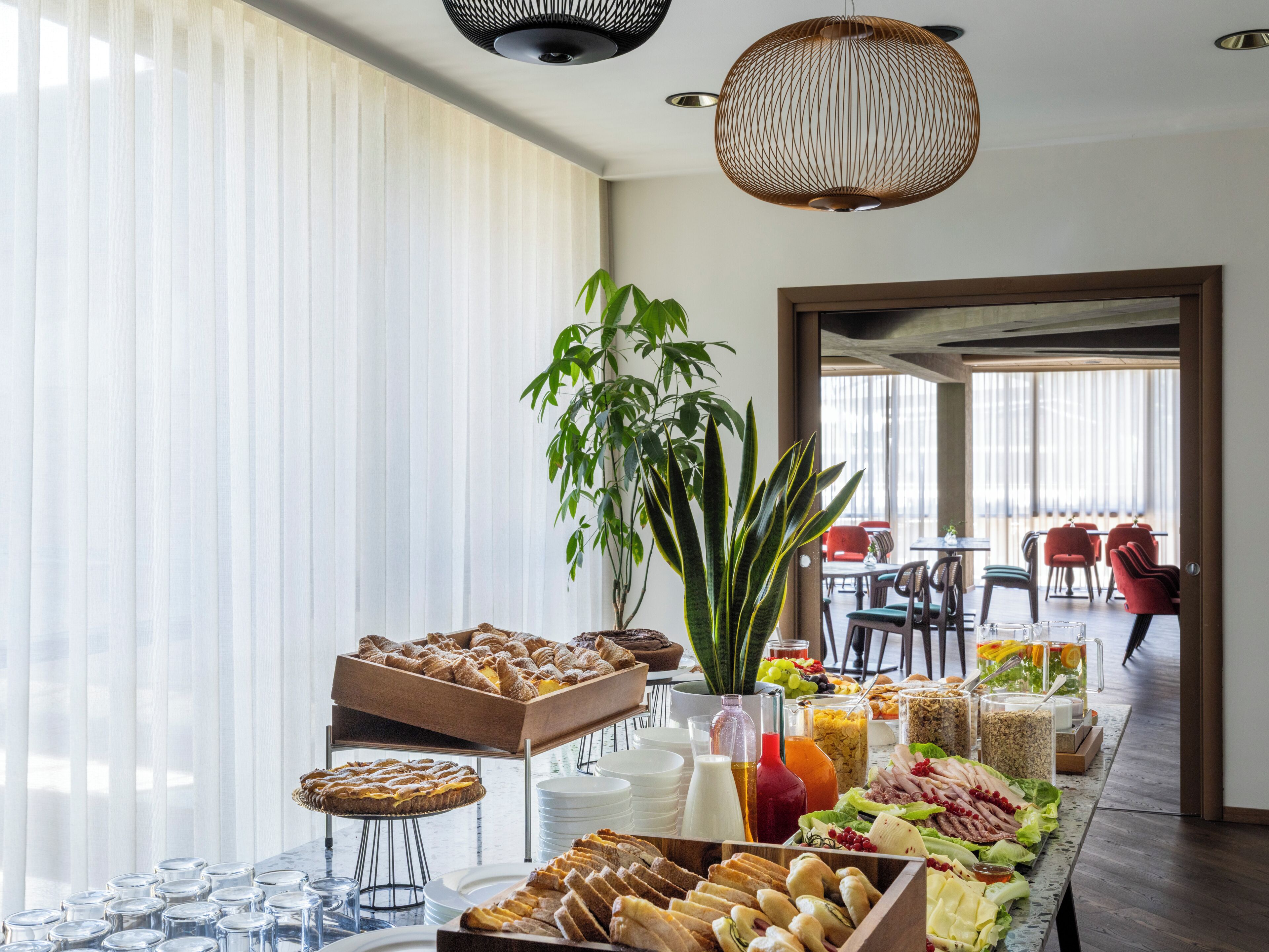 Un bufé con diversos alimentos, una planta grande y un comedor con sillas rojas.