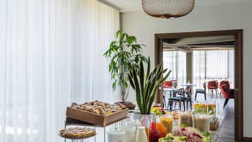 Un bufé con diversos alimentos, una planta grande y un comedor con sillas rojas.