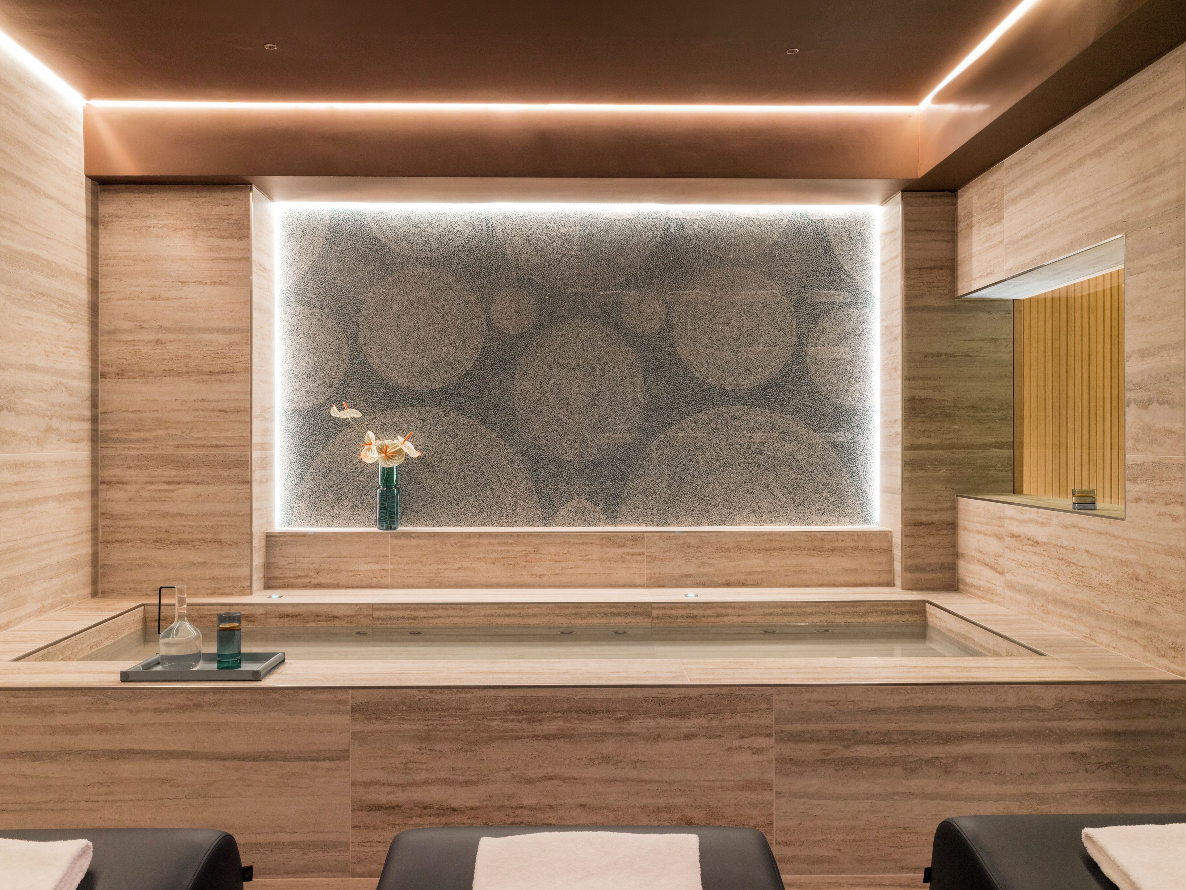Un baño moderno con un espejo grande, separador de vidrio y un florero con flores.