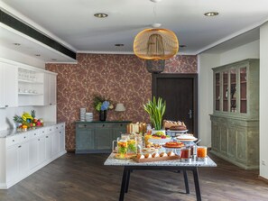 Un espace repas doté d’un comptoir en marbre, d’une variété de plats et de boissons, d’une suspension décorative et d’un papier peint à motifs.