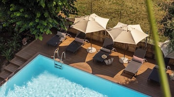 Una piscina con sillas de descanso y sombrillas, rodeada de vegetación.